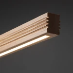 Czarna lampa sufitowa LED Viga Wood o mocy 14W i barwie 3000K, z elementem w kolorze sosny. Widoczny detal z gładkiego drewna z wypustkami, wzdłuż którego znajduje się wąski pasek światła. Produkt prezentowany w zbliżeniu, na ciemnym tle.