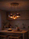 Beżowa lampa wisząca Sisu Round z trzema źródłami światła E27, zawieszona na długich przewodach. Lampy mają okrągłe klosze, emitujące ciepłe światło, w otoczeniu nowoczesnej kuchni z drewnianymi meblami i dekoracjami.