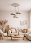 Beżowa lampa wisząca Sisu Round z trzema kloszami, zawieszona na długich przewodach z metalowym wykończeniem. Umieszczona w nowoczesnym wnętrzu, obok jasnej sofy i drewnianego stołu, tworzy przytulną atmosferę.