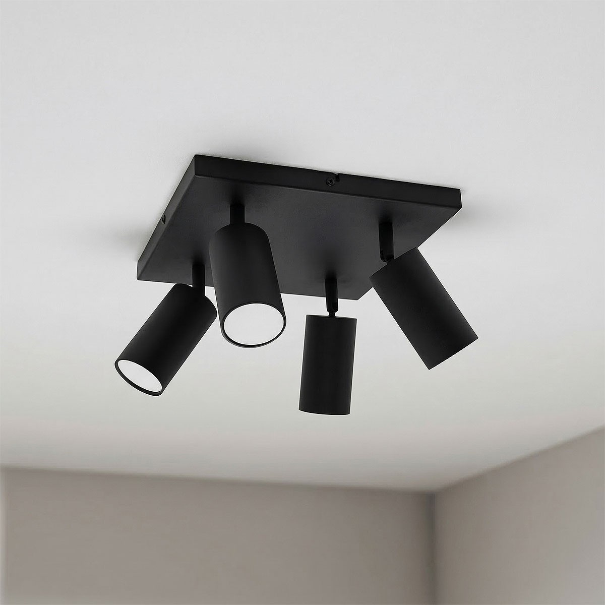 Czarna sufitowa lampa typu spot z czterema reflektorami GU10, zamontowana na kwadratowej płycie. Reflektory mają cylindryczny kształt, skierowane w różnych kierunkach, co pozwala na regulację oświetlenia w pomieszczeniu.