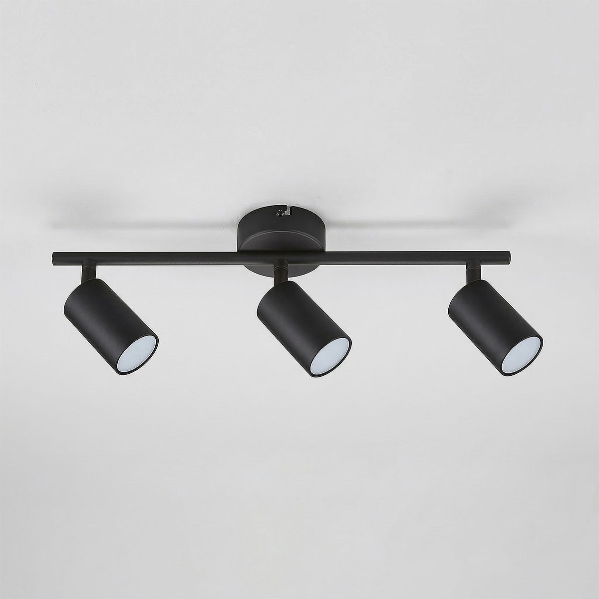 Czarna lampa sufitowa Stico z trzema reflektorami GU10, zamontowana na prostokątnej podstawie. Reflektory mają cylindryczny kształt i są skierowane w dół, co umożliwia regulację kierunku światła. Tło jasne, proste.