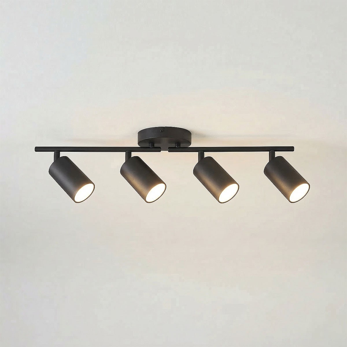 Czarna lampa sufitowa Stico z czterema reflektorami GU10, umieszczona na prostokątnej podstawie. Reflektory mają cylindryczny kształt, są ustawione w różnych kierunkach, co umożliwia skierowanie światła w pożądane miejsca. Tło jasne.