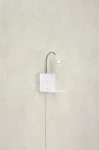 Kinkiet Cuarto w kolorze białym z portem USB, z elastycznym ramieniem i lampą GU10. Montowany na ścianie, z prostokątną podstawą i małą półką. W zestawie widoczne przewody elektryczne. Tło w odcieniu szaro-beżowym.
