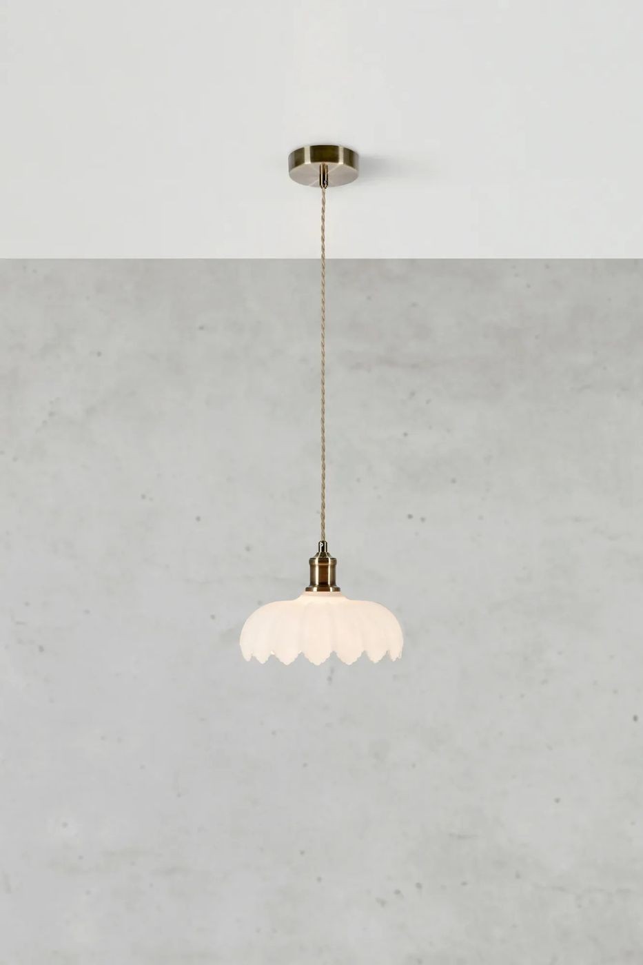 Lampa wisząca Kurage E27 w kolorze antycznego mosiądzu z białym kloszem w kształcie kwiatowym. Zawieszona na cienkim przewodzie, z montażem sufitowym. Tło w odcieniu szarym, minimalistyczne.