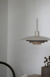 Piny lampa wisząca E27 w kolorze beżowym, z okrągłym kloszem o dwóch warstwach, zawieszona na białym przewodzie. Widoczna w minimalistycznym wnętrzu, obok filiżanki i doniczki z rośliną. Kąt ujęcia z boku, ukazujący detal oraz nowoczesny design.