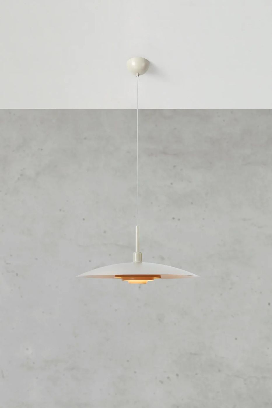 Lampa wisząca E27 w kolorze beżowym, z metalowym kloszem o okrągłym kształcie, zawieszona na cienkim przewodzie. Widoczna wnętrze klosza w odcieniu złotym, montowana do sufitu. Tło w odcieniach szarości.