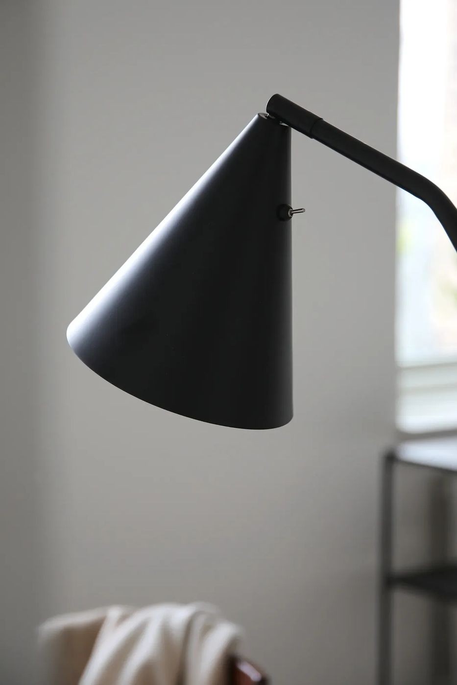 Czarna lampa podłogowa LED Funil o mocy 4,9W, z charakterystycznym stożkowym kloszem, z bliska ukazuje gładką, matową powierzchnię oraz ruchomy ramion, umieszczona w minimalistycznym wnętrzu.