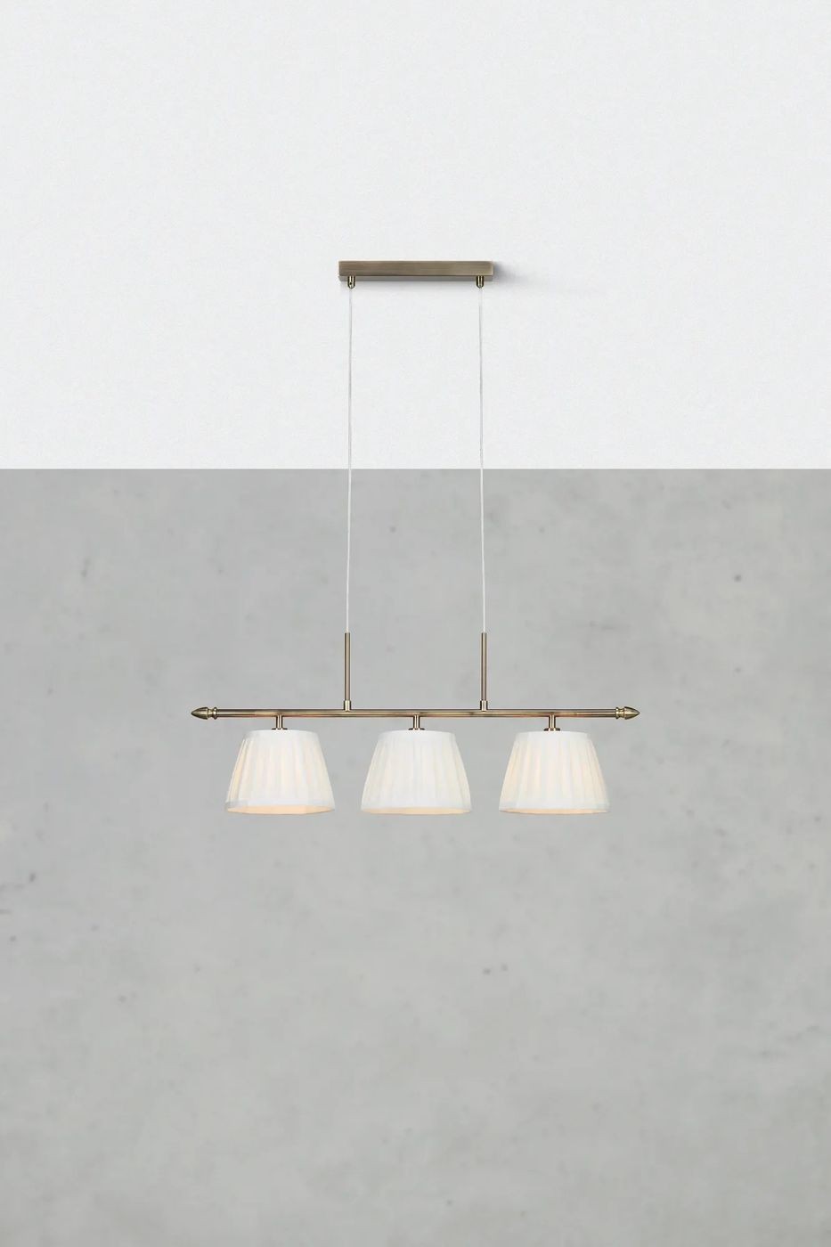Lampa wisząca Oxford z antycznego mosiądzu, z trzema kloszami w kształcie stożków. Klosze w kolorze białym, z delikatnym żłobieniem. Produkt zawieszony na metalowym stelażu, z dwiema przezroczystymi linkami, w aranżacji na jednolitym tle.
