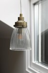 Lampa wisząca Bellis E14 w antycznym mosiądzu z przezroczystym, fakturowanym kloszem. Ujęcie z boku, widoczny detal oprawy oraz żarówki. Klosz ma kształt stożka z wyraźnymi żłobieniami, zawieszony na przezroczystym przewodzie.