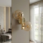 Kinkiet Eral z dwoma kloszami E14, w kolorze błyszczącego złota. Montowany na ścianie, pokazany w zbliżeniu. Klosze mają okrągły kształt, przezroczystą fakturę, a całość umieszczona w nowoczesnym wnętrzu z oknem w tle.