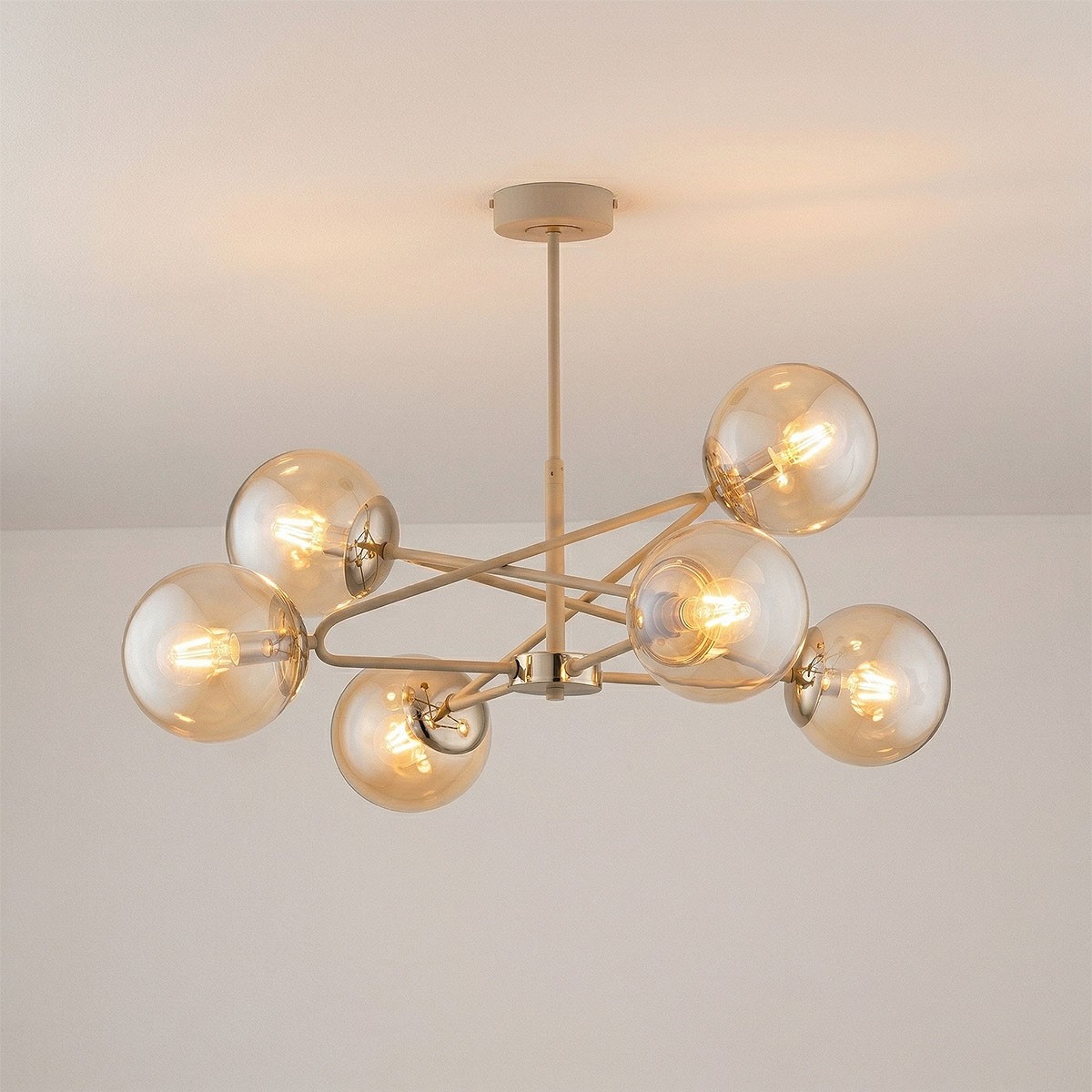 Lampa wisząca Sagito 6xE14 w kolorze beżowym z metalowymi elementami w złotym odcieniu. Posiada sześć przezroczystych kulistych kloszy, zamontowana na długim, prostym stelażu. Widok z dołu, na jasnym tle.