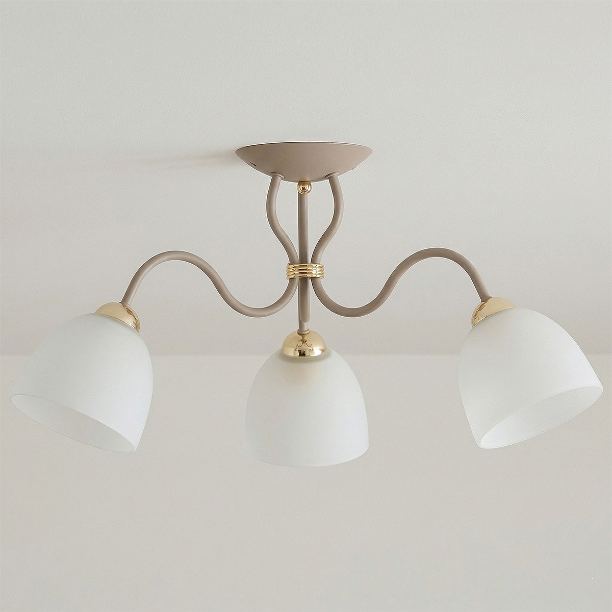 Lampa sufitowa Ariel z trzema kloszami E27 w kolorze taupe i złotej metalowej oprawie. Klosze mają zaokrąglony kształt i matowe wykończenie, a całość zamontowana jest na stelażu z falistymi ramionami.