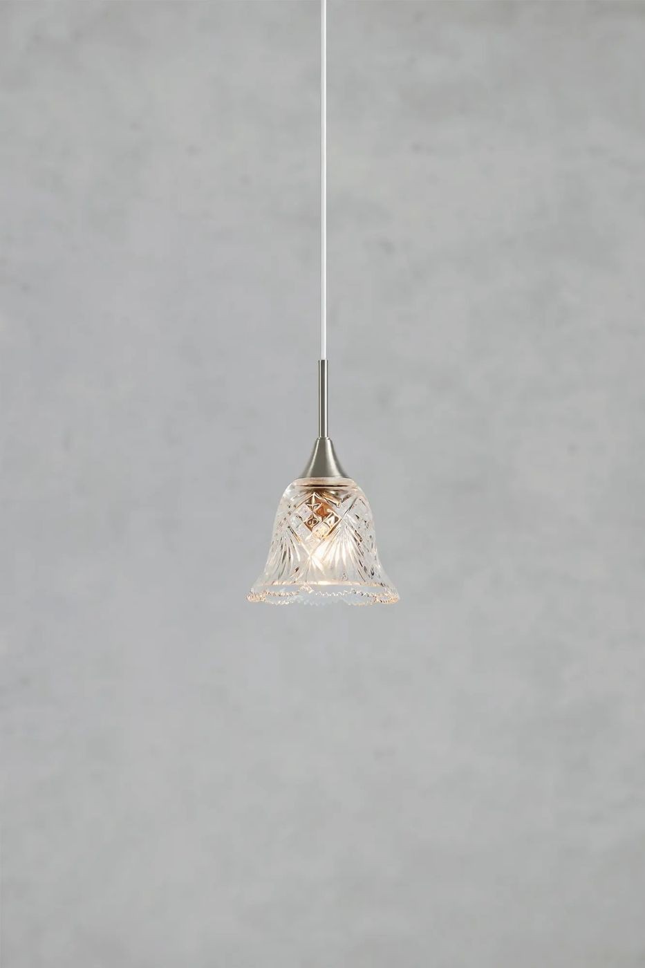 Lampa wisząca Luna E14 o niklowanym wykończeniu w kolorze satynowym, z kloszem w formie dzwonu z przezroczystego szkła z dekoracyjnym wzorem. Produkt zawieszony na białym przewodzie, widoczny z boku, na jednolitym tle.