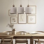 Beżowa lampa wisząca Amura z trzema kloszami w kształcie cylindrów, wykonana z lnu. Zawieszona na długich przewodach w prostym, eleganckim wnętrzu z drewnianym stołem i obrazami na ścianie.