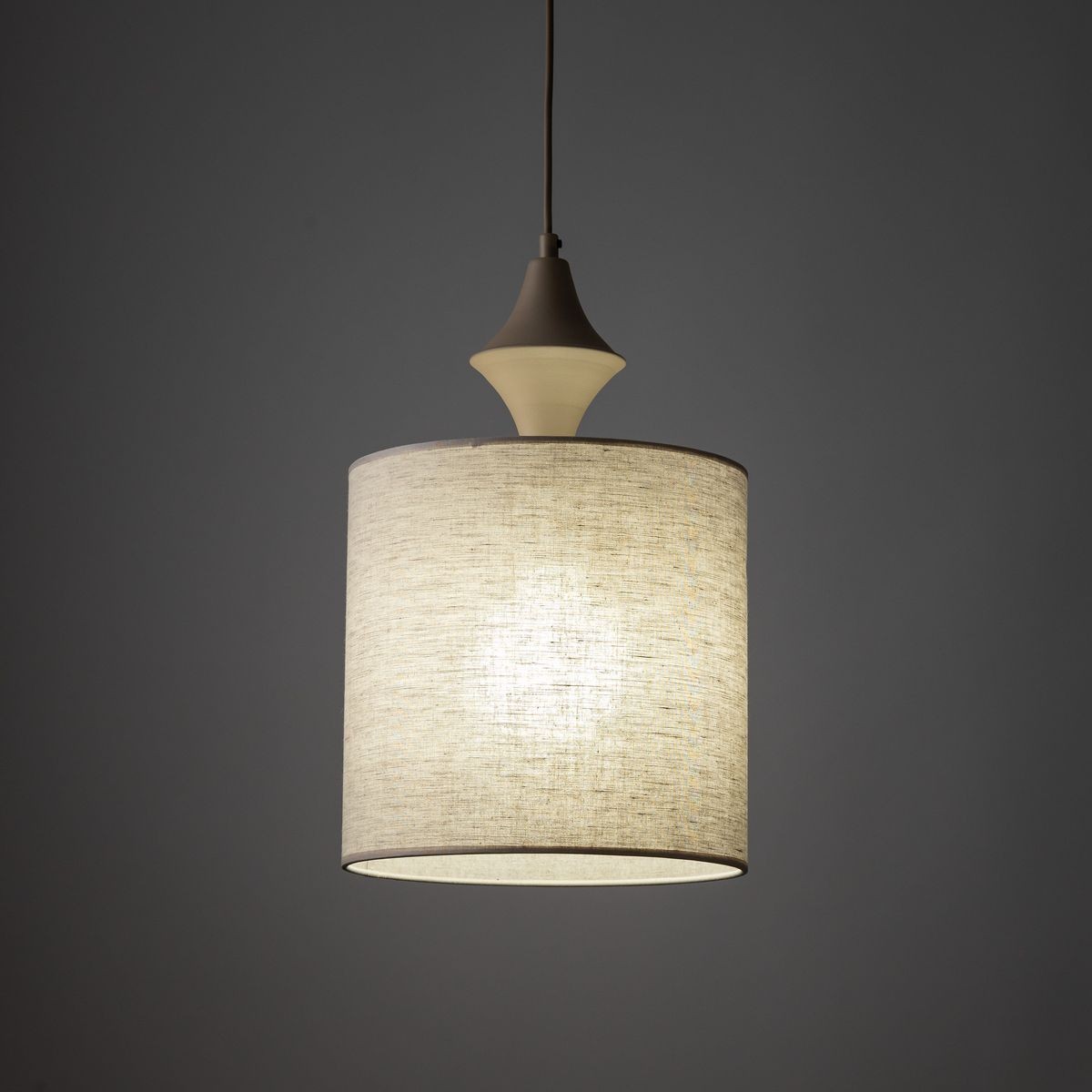 Lampa wisząca Amura 1xE27 w kolorze beżowym, z okrągłym kloszem z lnu, zawieszona na cienkim przewodzie. Górna część z dekoracyjnym detalem w kształcie stożka. Tło jednolite, ciemne.