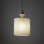 Lampa wisząca Amura 1xE27 w kolorze beżowym, z okrągłym kloszem z lnu, zawieszona na cienkim przewodzie. Górna część z dekoracyjnym detalem w kształcie stożka. Tło jednolite, ciemne.