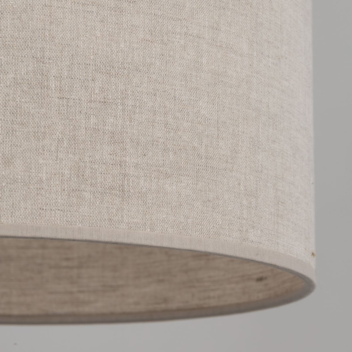 Beżowa lampa wisząca Amura z materiału lnianego, z okrągłym abażurem. Widoczna tekstura tkaniny, delikatne wykończenie krawędzi. Lampa przeznaczona na żarówkę E27, w ujęciu zbliżeniowym na detal abażura.