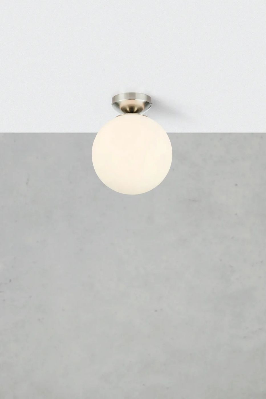 Lampa sufitowa Stintino z oprawą w kolorze niklu satynowego. Okrągła, mleczna kula z tworzywa, zamontowana na suficie. Prosty design, idealna do nowoczesnych wnętrz. Tło w odcieniach szarości.