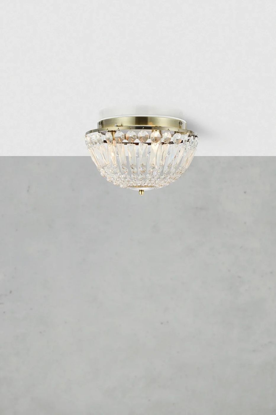 Lampa sufitowa Estelle w antycznym mosiądzu z kryształowym kloszem, zamontowana na suficie. Klosz ma okrągły kształt z wycięciami, które rozpraszają światło. Produkt o eleganckim designie, przeznaczony do oświetlenia wnętrz.