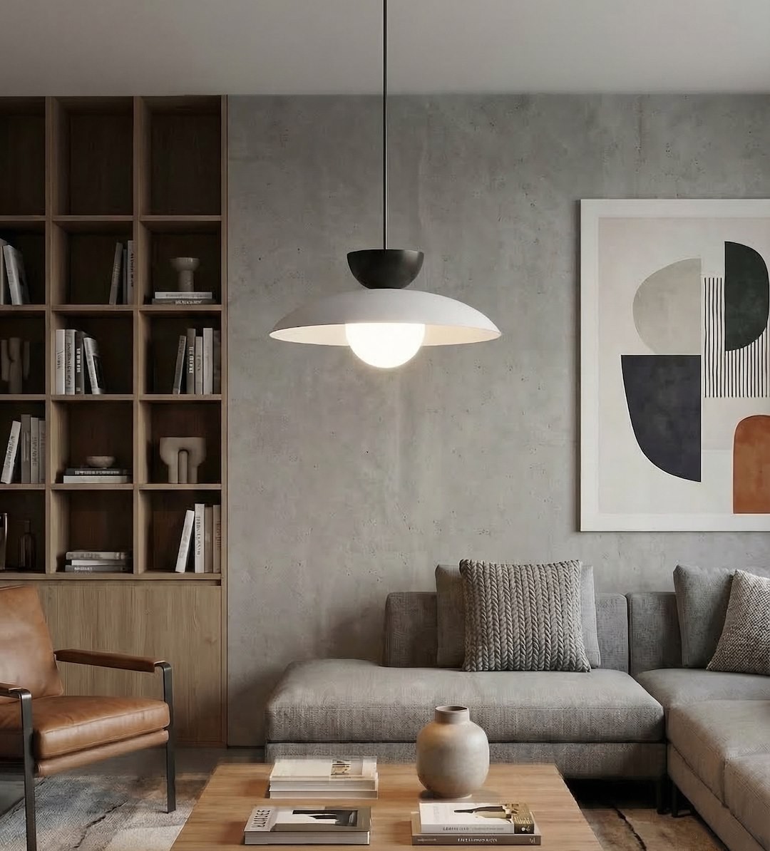 Lampa wisząca Mulan w kolorze szarym i czarnym z jednym źródłem światła G9, umieszczona nad stolikiem w nowoczesnym wnętrzu. Okrągła, matowa czasza z białym wykończeniem, zawieszona na cienkim, czarnym przewodzie. W tle drewniana półka z książkami.