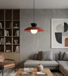 Lampa wisząca Mulan 1xG9 w kolorze burgundowym i czarnym, z okrągłym białym kloszem. Zawieszona na cienkim kablu, w aranżacji nowoczesnego salonu z drewnianymi regałami i szaro-beżową kanapą. W tle widoczna dekoracja ścienna.