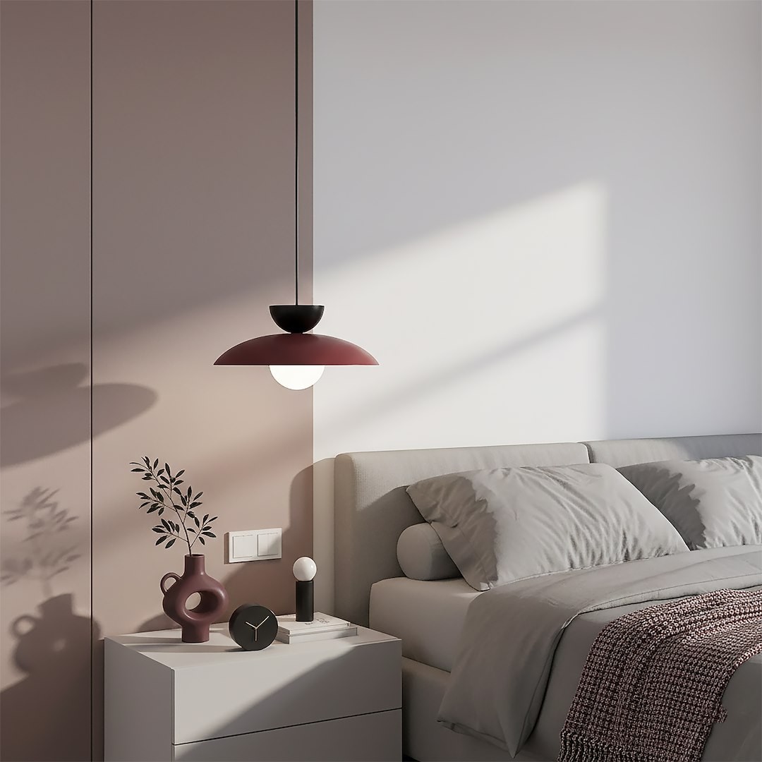 Lampa wisząca Mulan w kolorze burgundowym i czarnym z białą kulą, zawieszona nad białą szafką nocną w sypialni. Obok znajdują się dekoracyjne akcesoria: wazon, zegar oraz lampka, a na ścianie widoczny jest delikatny cień.