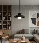 Lampa wisząca Mulan w kolorze czarnym, z jedną żarówką G9. Okrągła, matowa oprawa z białym kloszem, zawieszona na cienkim kablu. W tle nowoczesny salon z regałem, sofą i stolikiem kawowym.