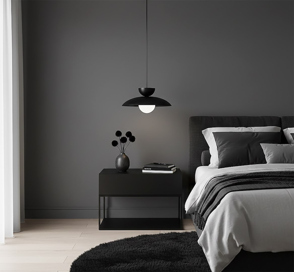 Lampa wisząca Mulan w kolorze czarnym z oprawą G9, zawieszona nad nocnym stolikiem. W tle szare ściany, na stoliku wazon z czarnymi kwiatami oraz kilka książek. Wnętrze nowoczesne, z wyraźnymi kontrastami.