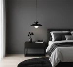 Lampa wisząca Mulan w kolorze czarnym z oprawą G9, zawieszona nad nocnym stolikiem. W tle szare ściany, na stoliku wazon z czarnymi kwiatami oraz kilka książek. Wnętrze nowoczesne, z wyraźnymi kontrastami.
