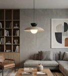 Lampa wisząca Mulan w kolorze mokka i czarnym, z jedną oprawą G9. Okrągła, matowa czasza z białym kloszem, zwisająca z cienkiego, czarnego kabla. W tle nowoczesny salon z szaro-beżowymi ścianami i drewnianymi meblami.