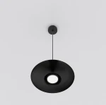 Lampa wisząca Babel 1xGX53 w kolorze czarnym, o okrągłym kształcie z centralnym otworem na źródło światła. Zawieszona na cienkim przewodzie, prezentuje minimalistyczny design. Tło jasne, co podkreśla elegancję lampy.