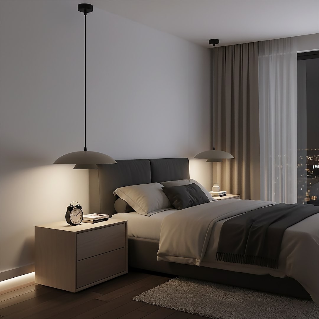 Lampa wisząca Babel 1xGX53 w kolorze czarnym i mokka, zawieszona nad łóżkiem w sypialni, z minimalistycznym kloszem. W otoczeniu jasne meble, poduszki i zegar na stoliku nocnym, z zasłonami w odcieniach beżu.