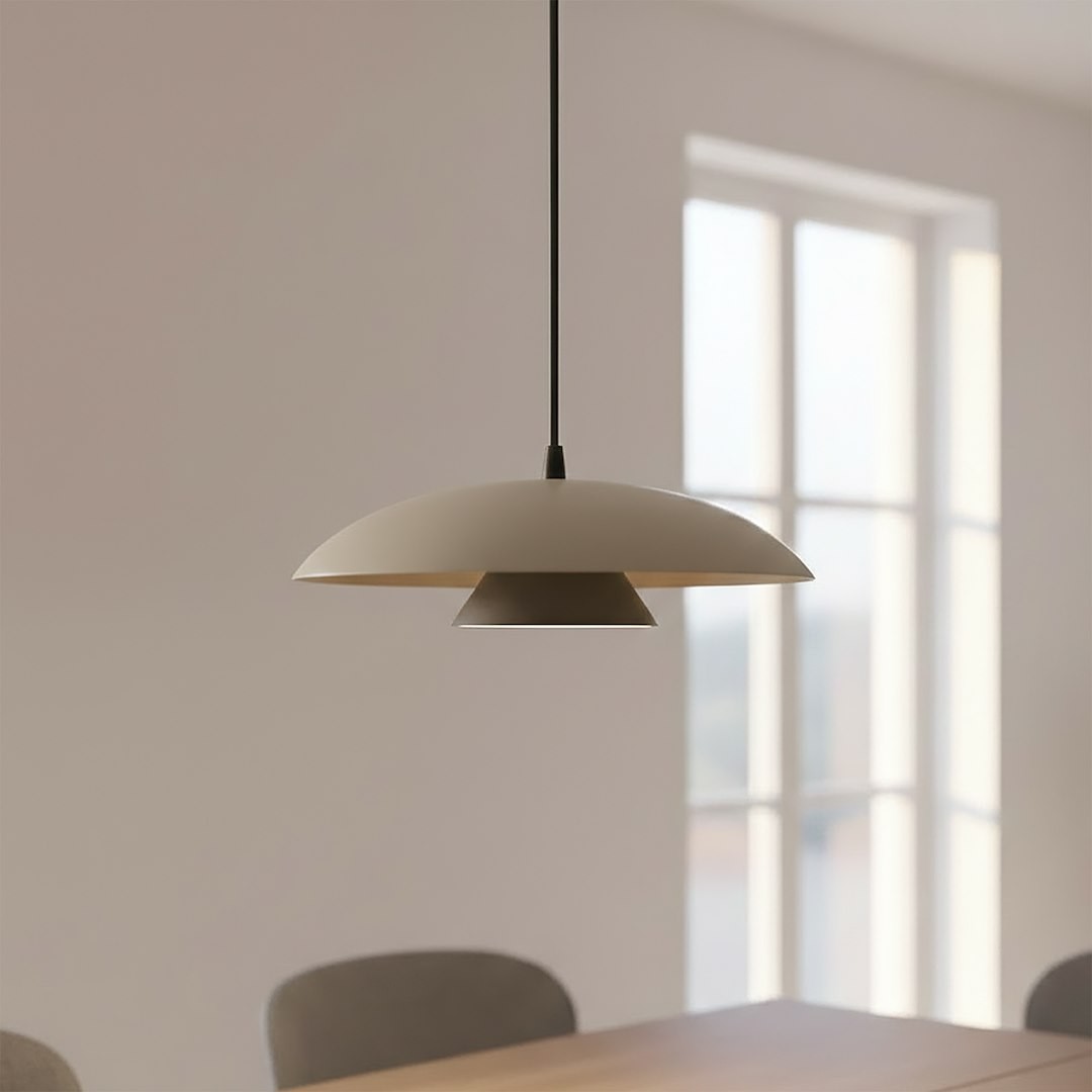 Lampa wisząca Babel 1xGX53 w kolorze czarnym i mokka, o zaokrąglonym kloszu zewnętrznym i stożkowym elementem wewnętrznym. Zawieszona na cienkim, czarnym przewodzie, w jasnym wnętrzu z oknami.