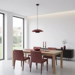 Lampa wisząca Babel w kolorze czarnym i burgundowym, z pojedynczym źródłem światła GX53, zawieszona nisko nad drewnianym stołem w nowoczesnej jadalni. W tle widoczne burgundowe krzesła, czarne meble i naturalne światło wpadające przez okna.