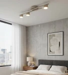 Fragment lampy sufitowej 3xGX53 w kolorze mokka, zamontowanej na suficie. Lampa składa się z trzech okrągłych źródeł światła umieszczonych na prostokątnej podstawie. W tle widoczne wnętrze sypialni z szaro-białymi ścianami i oknem.