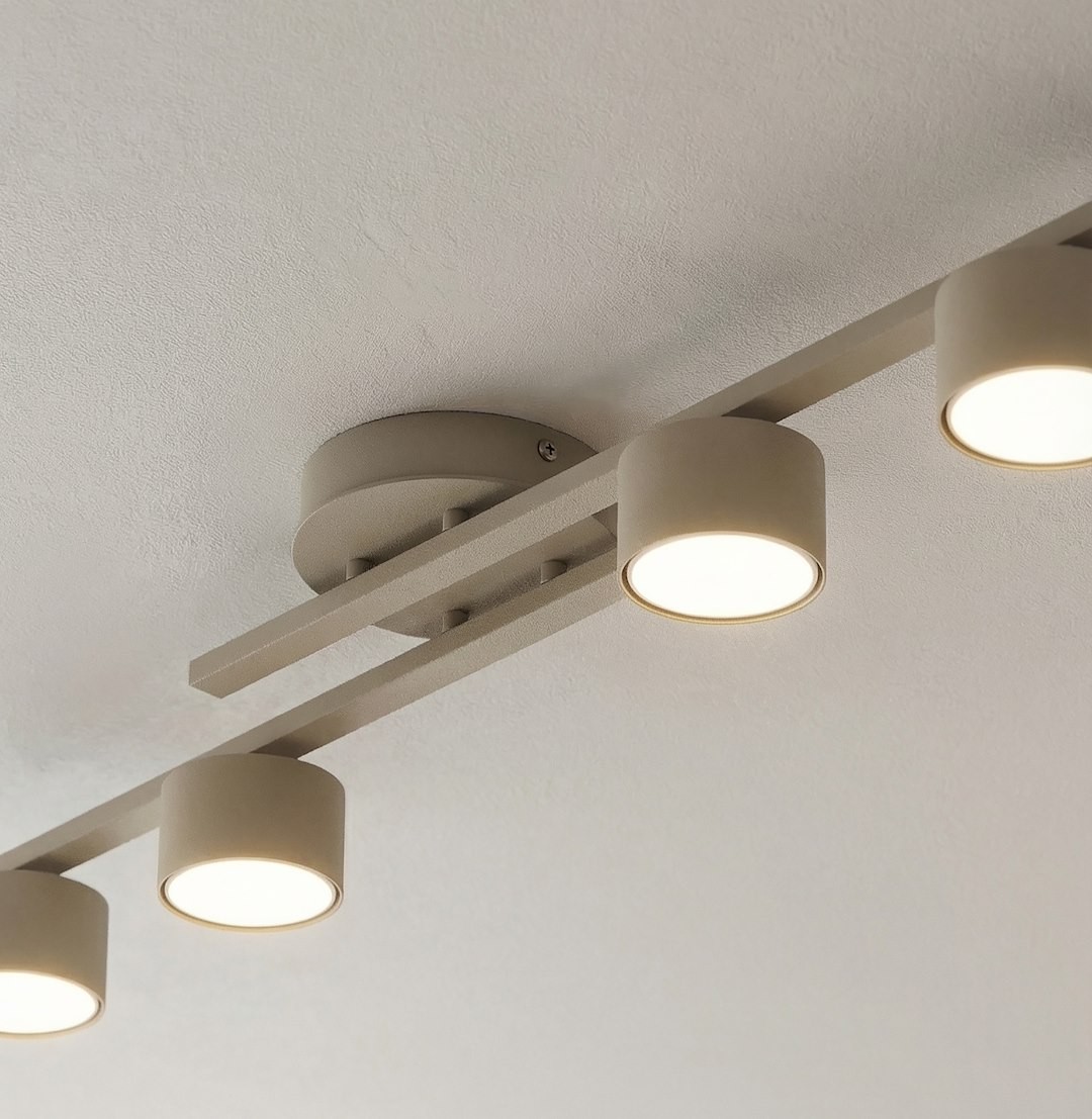 Fragment lampy sufitowej 4xGX53 w kolorze mokka, z metalową konstrukcją i okrągłymi kloszami. Ujęcie z góry, ukazujące zamontowane na suficie źródła światła. Klosze mają jasne, emitujące światło wnętrze, utrzymane w minimalistycznym stylu.