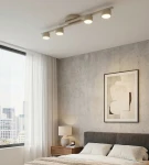 Fragment lampy sufitowej 4xGX53 w kolorze mokka, zamontowanej na suficie. Oświetlenie składa się z czterech okrągłych, białych kloszy. W tle widoczna sypialnia z szarymi ścianami, oknem i meblami.