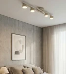 Lampa sufitowa 4xGX53 w kolorze mokka, zamontowana na suficie, z czterema okrągłymi źródłami światła. Ujęcie z boku, w tle widoczna sypialnia z łóżkiem, poduszkami i zasłonami. Ściana o fakturze betonu, minimalistyczne dekoracje.