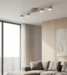 Fragment lampy sufitowej 4xGX53 w kolorze mokka, zamontowanej na suficie, z widocznymi czterema okrągłymi kloszami emitującymi światło. Lampa znajduje się w nowoczesnym wnętrzu z szaro-beżową sofą i dużymi oknami.