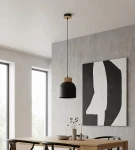 Lampa wisząca Vigo 1xE27 w kolorze czarnym z drewnianym detalem na górze, zawieszona na cienkim kablu. Umieszczona nad drewnianym stołem, w minimalistycznym wnętrzu z betonową ścianą i abstrakcyjnym obrazem w tle.