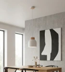 Lampa wisząca Vigo w kolorze białym z drewnianym detalem u góry, zawieszona na cienkim przewodzie. Produkt umieszczony w nowoczesnym wnętrzu z betonową ścianą i drewnianym stołem, w otoczeniu okien i dekoracji.