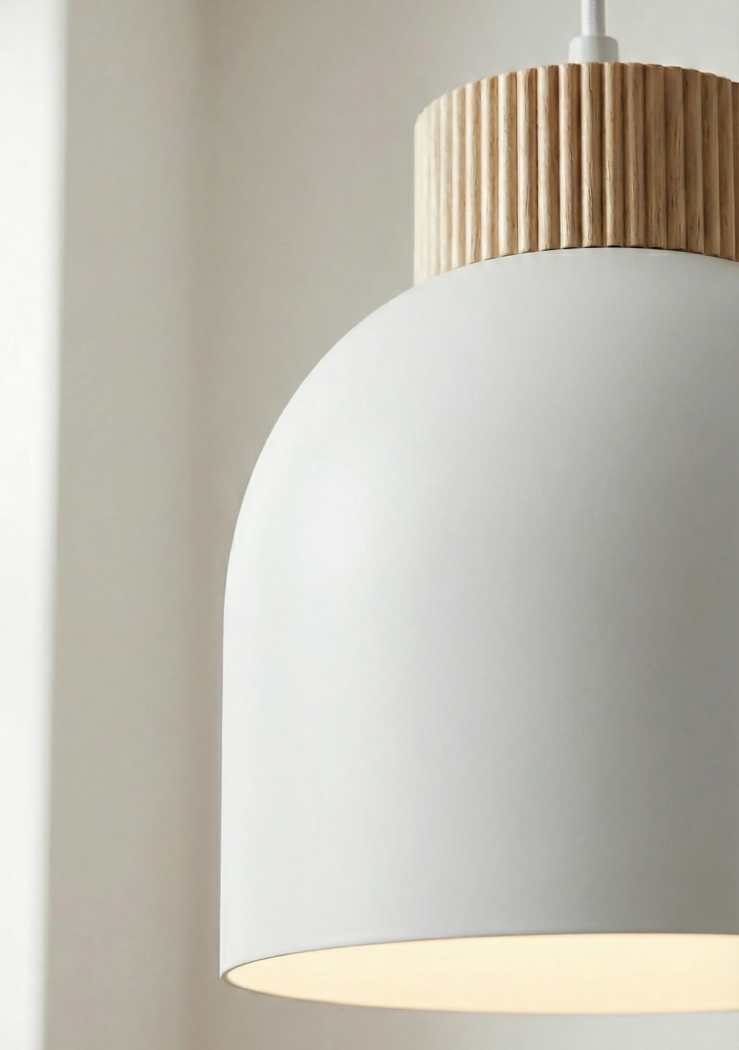 Lampa wisząca Vigo w kolorze białym z oprawą z drewna, posiada okrągły kształt. Ujęcie zbliżeniowe na detal lampy, widoczny górny, żłobiony element z drewna. Widoczne miejsce na żarówkę E27. Idealna do nowoczesnych wnętrz.