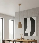 Lampa wisząca Vigo w kolorze mokka z kloszem w kształcie stożka i drewnianym detalem u góry, zawieszona na długim przewodzie. W tle widoczny stół z kwiatami w wazonie oraz abstrakcyjny obraz na ścianie.