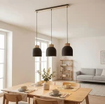 Lampa wisząca Vigo 3xE27 w kolorze czarnym z drewnianymi detalami, zawieszona na długich przewodach. Trzy klosze w kształcie dzwonu, w aranżacji jadalni z drewnianym stołem i krzesłami. Jasne, neutralne tło z oknami i regałem.