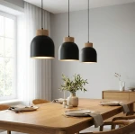 Lampa wisząca Vigo 3xE27 w kolorze czarnym z drewnianymi detalami, zawieszona nad stołem w nowoczesnej jadalni. Trzy lampy o zaokrąglonym kształcie, wiszące na cienkich, czarnych kablach. Otoczenie jasne, z drewnianym stołem i dekoracjami.