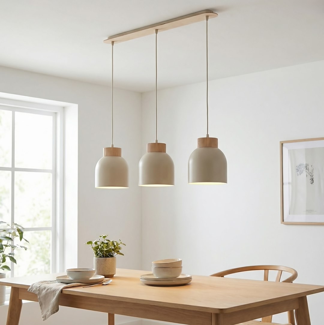Lampa wisząca Vigo 3xE27 w kolorze mokka, z trzema lampionami o zaokrąglonym kształcie, zawieszona na drewnianej podstawie. W tle stół z talerzami i doniczka z rośliną, na jasnym tle z oknem.