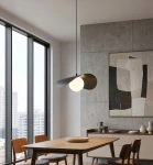 Czarna lampa wisząca Ritual M z kloszem w kształcie owalu i białym źródłem światła, zawieszona na cienkim przewodzie, w nowoczesnej aranżacji jadalni z drewnianym stołem i minimalistycznymi meblami. Tło z szarym betonem i dużymi oknami.