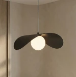 Czarna lampa wisząca Ritual L z jedną oprawą G9, z abażurem w kształcie dwóch skrzydełek, zawieszona na cienkim kablu. W centralnej części znajduje się okrągła, matowa żarówka, na tle jasnej, gładkiej ściany.