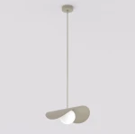 Lampa wisząca Ritual M w kolorze mokka z jedną oprawą G9. Posiada asymetryczny klosz w kształcie falującego liścia, z białą, okrągłą żarówką. Zamontowana na cienkim, metalowym przewodzie, zawieszona z sufitu na jednolitym, jasnym tle.