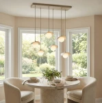 Lampa wisząca Ritual 6xG9 w kolorze mokka, z sześcioma kloszami w kształcie kwiatu, zawieszona na prostokątnej podstawie, umieszczona nad okrągłym stołem w jasnym wnętrzu. Tło z dużymi oknami i zielonym otoczeniem.